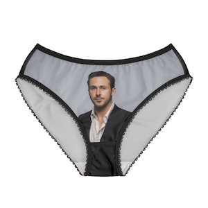 May include: White underwear with a black lace trim and a portrait of a man in a suit. The underwear has a gray background and a black trim around the waist.
