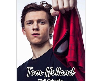 May include: A wall calendar featuring Tom Holland, known for his role as Spider-Man, holding a red and blue Spider-Man costume. The text "Tom Holland Wall Calendar" is printed below the image.