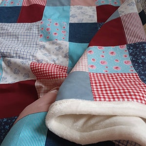 Könnte beinhalten: Eine Patchwork-Decke mit verschiedenen floralen und geometrischen Mustern in Blautönen, Rot, Weiß und Rosa. Die Decke besteht aus verschiedenen Stoffen und hat ein weiches, flauschiges weißes Futter.