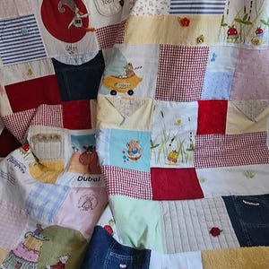 Könnte beinhalten: Eine Patchwork-Decke aus verschiedenen Stoffen mit einer Vielzahl von Farben und Mustern, darunter Rot, Blau, Gelb und Grün. Die Decke besteht aus Quadraten und Rechtecken, und einige der Quadrate haben gestickte Designs. Die Decke ist in der Hälfte gefaltet und liegt auf einem Holzboden.