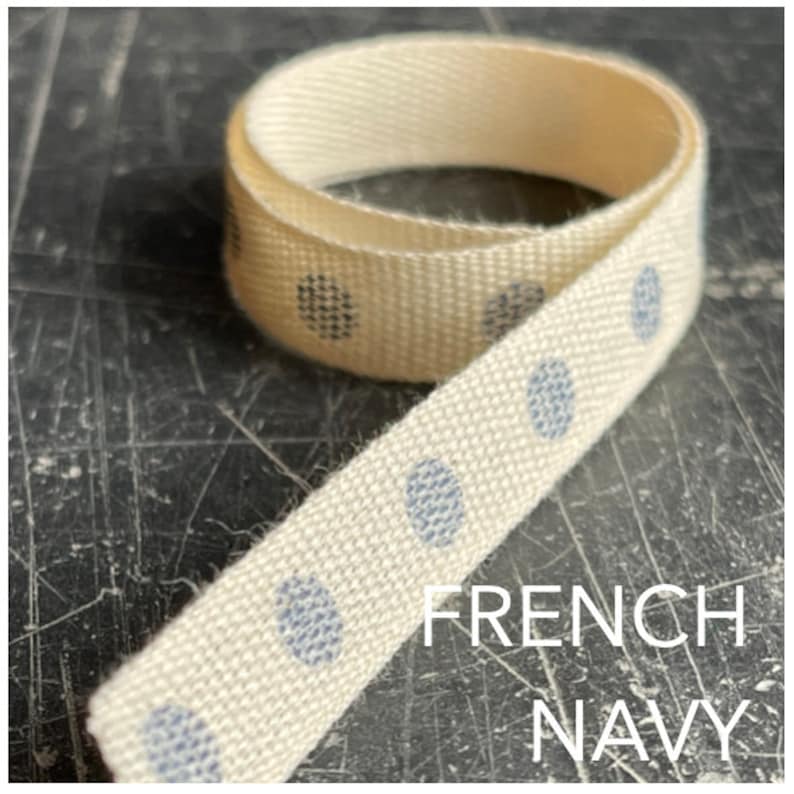 May include: A close-up of a white cotton ribbon with blue polka dots. The ribbon is rolled up and the text "FRENCH NAVY" is visible below the ribbon.