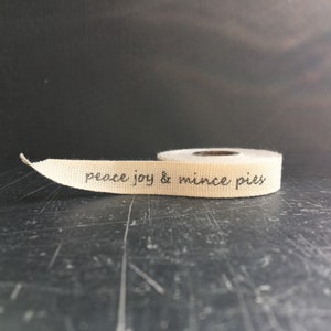 May include: A roll of natural coloured fabric ribbon with the text "peace joy & mince pies" printed in black ink.