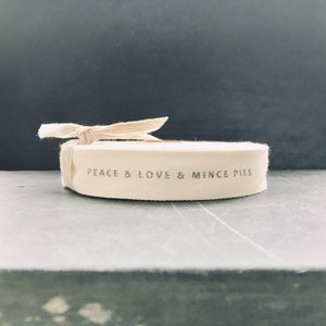 May include: A white cotton ribbon with the text "Peace & Love & Mince Pies" printed on it.