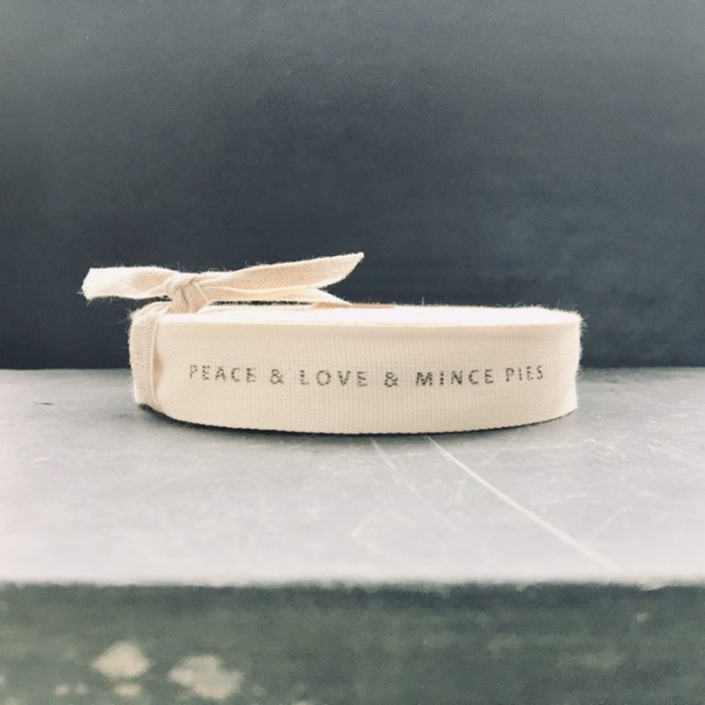 May include: A white cotton ribbon with the text "Peace & Love & Mince Pies" printed on it.