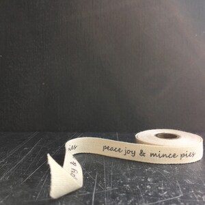 May include: A roll of natural coloured fabric ribbon with the text "peace joy & mince pies" printed in black ink.
