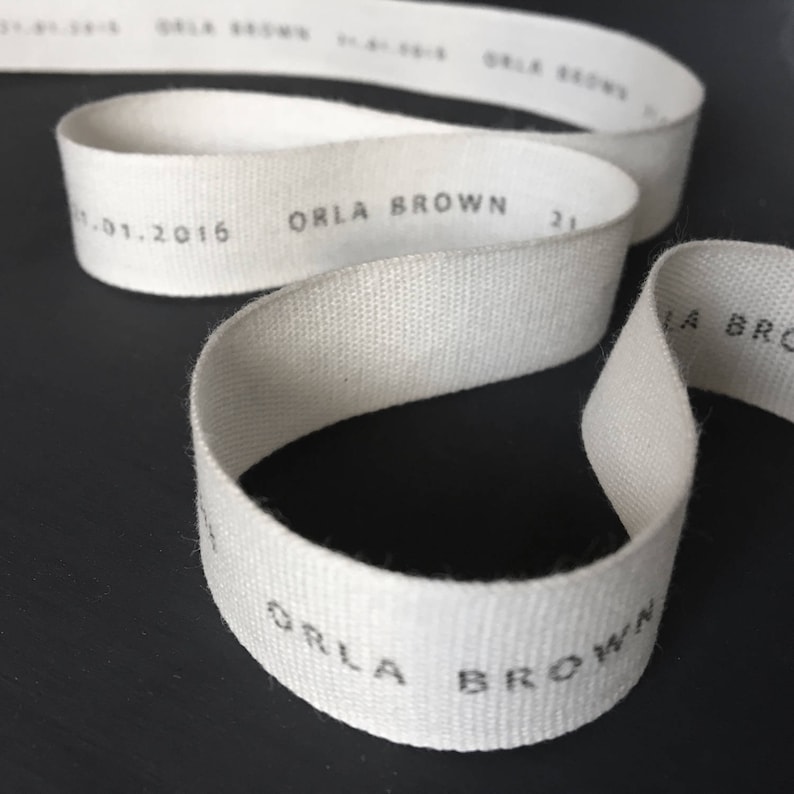 May include: White cotton ribbon with the text "ORLA BROWN" printed in black. The ribbon is folded in a loop.