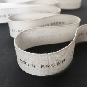 May include: White cotton ribbon with the text "Orla Brown" printed in black.
