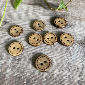 May include: Eight brown wooden buttons with two holes each. The buttons have a stitched edge and a light brown centre.
