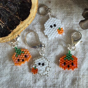 May include: Four Halloween-themed beaded charms with silver keychains. Two charms are white ghosts with black eyes and orange pumpkins. Two charms are orange pumpkins with green stems.