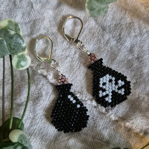 May include: A pair of black beaded earrings in the shape of potion bottles, with a skull design. The earrings have silver-colored lever-back closures and a pink beaded accent at the top of the bottle.