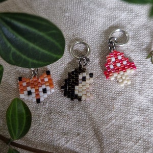 May include: Three beaded charms on silver rings. The charms are a red and white mushroom, a black and white hedgehog, and an orange and white fox.
