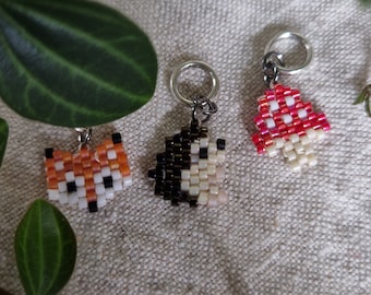 May include: Three beaded charms on silver rings. The charms are a red and white mushroom, a black and white hedgehog, and an orange and white fox.