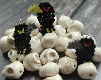May include: Three beaded raven pendants with yellow beaks and red eyes rest on a bed of white skull beads. The ravens are black with yellow and red accents. The skull beads have a marbled appearance.
