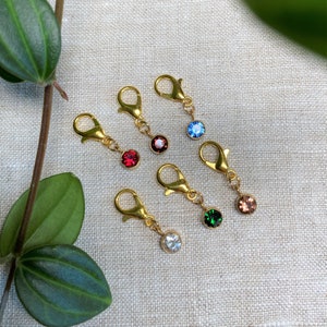 May include: Six gold stitch markers with different coloured crystal beads. The beads are red, blue, green, brown, white and clear.