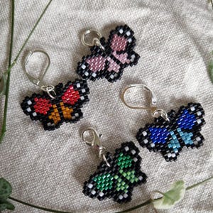May include: Four beaded butterfly keyrings with silver clasps. The butterflies are black with different coloured wings: pink, red and orange, blue and light blue, and green.