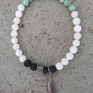 May include: A white and blue beaded bracelet with a black lava rock bead and a silver feather charm.