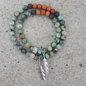 May include: A double-strand bracelet with green and brown beads, accented with silver feather charms and a silver bead.