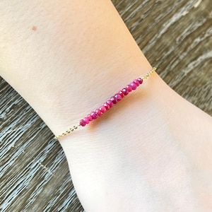 May include: A delicate gold chain bracelet with a row of small, pink gemstone beads.