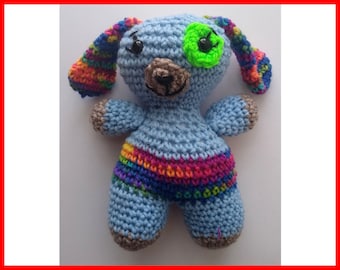 May include: A blue crocheted stuffed animal with a rainbow striped body and a green eye patch. The animal has a brown nose and black eyes.