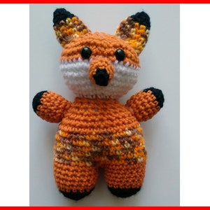 May include: A crocheted fox plush toy with orange, brown, and white fur. The fox has black eyes and a black nose.