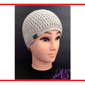 Könnte beinhalten: Eine graue Strickmütze mit einem strukturierten Muster. Die Mütze hat ein kleines blaues Etikett an der Seite.