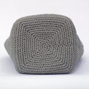 May include: A gray crocheted tote bag with a square bottom. The bag is made with a thick yarn and has a simple, classic design.