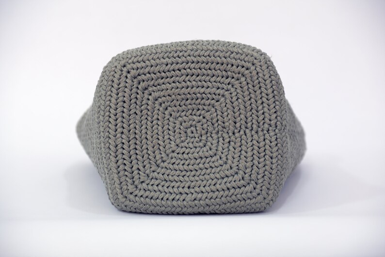 May include: A gray crocheted tote bag with a square bottom. The bag is made with a thick yarn and has a simple, classic design.