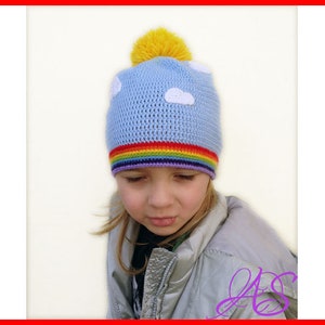 Könnte beinhalten: Hellblaue Häkelmütze mit weißen Wolkenapplikationen und einem gelben Bommel. Die Mütze hat ein Regenbogenband am unteren Rand. Die Mütze ist für Kinder konzipiert.