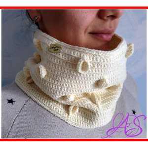 May include: A white crocheted neck warmer with a textured design and small, raised bumps. The neck warmer has a label with the letters "AS" on it.