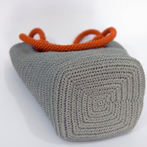May include: A gray crocheted tote bag with orange handles. The bag has a square bottom and a woven texture.