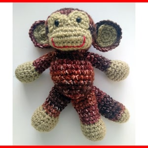 May include: A crocheted monkey toy with brown and beige yarn. The monkey has a red stitched smile and black eyes.