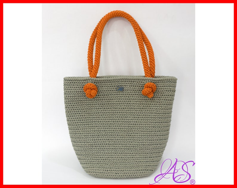 May include: A gray crocheted tote bag with orange rope handles. The bag has a slightly rounded bottom and a rectangular top.