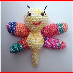 May include: A crocheted dragonfly toy with a yellow body, orange, pink, blue, and green wings, and black eyes.
