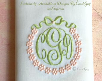 May include: A green embroidered monogram with a pearl and ribbon design. The monogram is surrounded by a circle of pink embroidered flowers. The text "Pearl & Ribbon Necklace Design Exclusively Available at Designs By Carol Guy on Etsy.com" is at the top of the image. The text "Carol Guy" is at the bottom of the image.