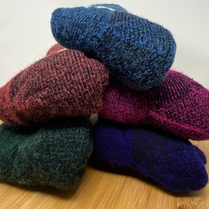 May include: A stack of five pairs of fuzzy socks in various colors, including blue, pink, red, green, and purple. The socks are folded and stacked on a wooden surface.
