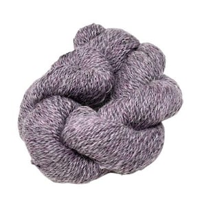 Puede incluir: Un ovillo de lana morada y gris, bien enrollado y anudado. El hilo tiene un aspecto texturizado, con fibras visibles y una mezcla de tonos claros y oscuros. El color general es un morado apagado con reflejos grises.