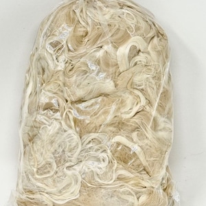 May include: A close-up of a plastic bag filled with a large amount of white and beige natural fibers. The fibers are loose and tangled, and they appear to be made of a soft, natural material.