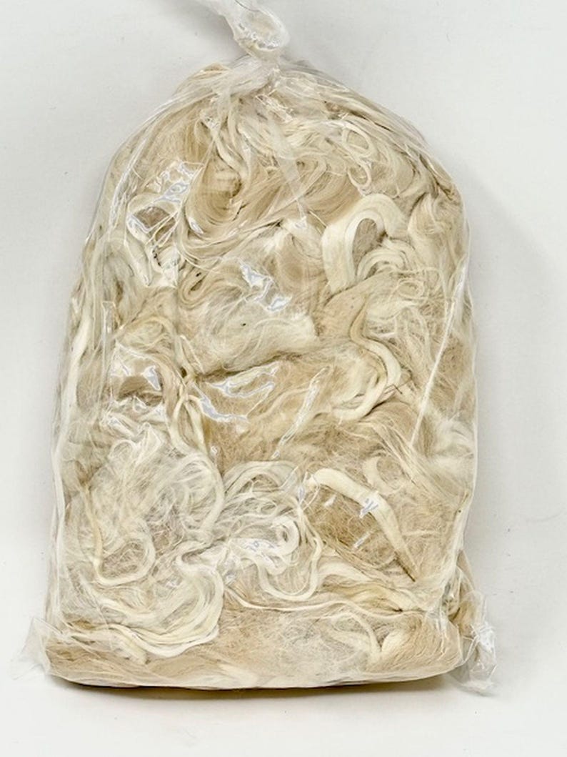 May include: A close-up of a plastic bag filled with a large amount of white and beige natural fibers. The fibers are loose and tangled, and they appear to be made of a soft, natural material.