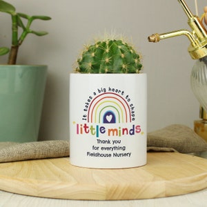 May include: White ceramic planter with a rainbow design and the text "It takes a big heart to shape little minds."  The planter also includes the text "Thank you for everything Fieldhouse Nursery".