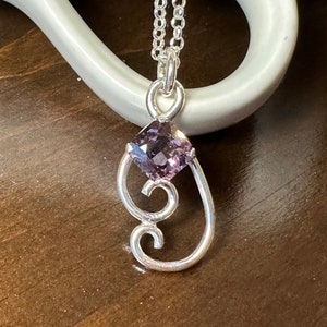 May include: A silver necklace with a delicate pendant featuring a purple gemstone and a swirling design.
