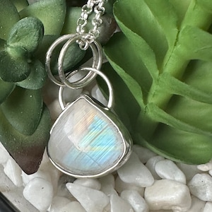 May include: A silver necklace with a teardrop-shaped moonstone pendant. The pendant has a rainbow iridescent sheen.