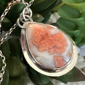 May include: A silver pendant necklace with a teardrop-shaped stone featuring a white and pink agate pattern.
