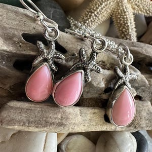 May include: Sterling silver earrings and necklace featuring pink teardrop-shaped stones. Each piece is adorned with a starfish accent. The jewelry is displayed on driftwood, evoking a coastal theme.