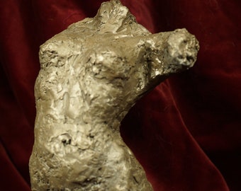 May include: A textured, abstract sculpture of a human torso made of a light brown material. The sculpture is posed with the arms raised and the head tilted back. The sculpture is displayed against a red velvet background.