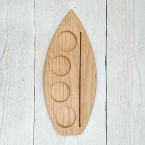 May include: A wooden serving tray with four circular indentations and a long, narrow groove down the center. The tray is shaped like a leaf and is made of light brown wood.