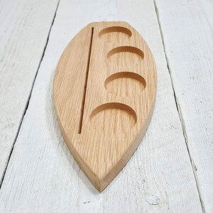 May include: A wooden serving tray shaped like a leaf with four circular indentations and a long, thin groove down the center.