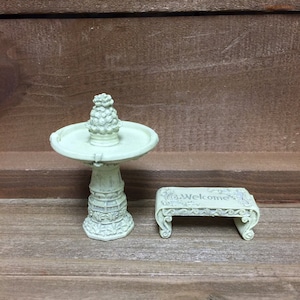 May include: A miniature green concrete fountain with a pineapple-shaped top and a matching green concrete bench with the word "Welcome" inscribed on it.