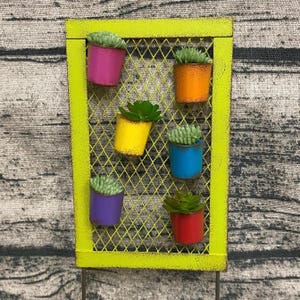 May include: A green metal grid wall planter with six small pots holding succulents. The pots are painted in different colors: pink, orange, yellow, blue, purple, and red.
