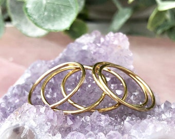 May include: Four gold stacking rings on a purple amethyst crystal cluster.
