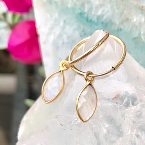 May include: Gold hoop earrings with a teardrop-shaped moonstone dangling from each hoop.